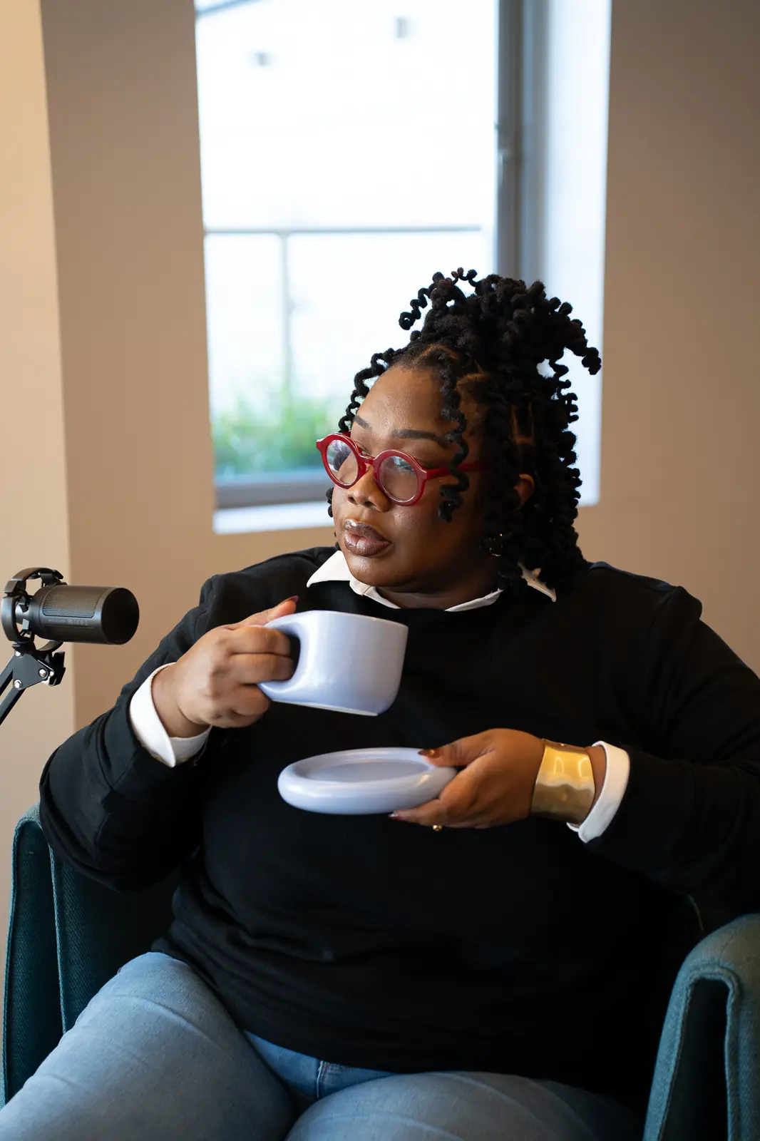 Norlander Wilson in red glasses holding a coffee cup beside a podcast microphone